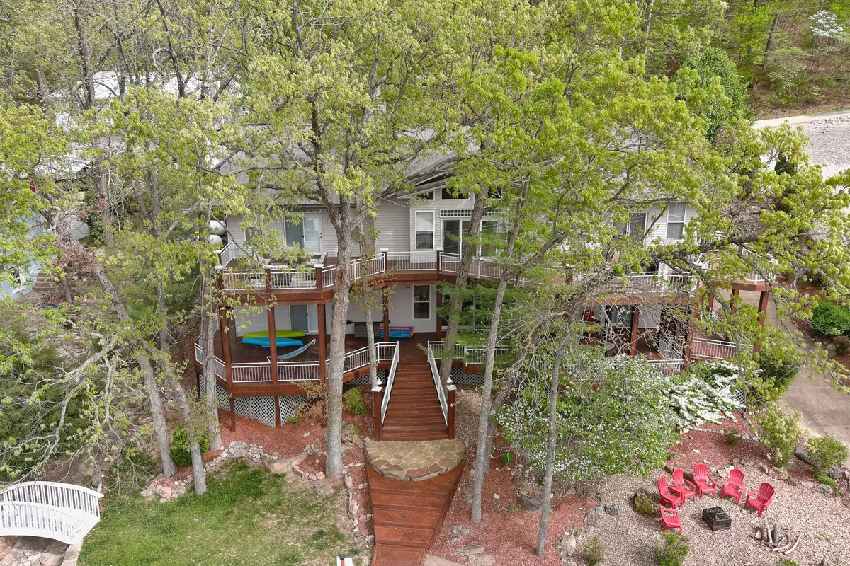 An expansive deck area with vibrant red chairs, lush greenery, and a winding walkway leading into the yard. The scene exudes tranquility while showcasing plenty of space for socializing, relaxing, or dining outside.
