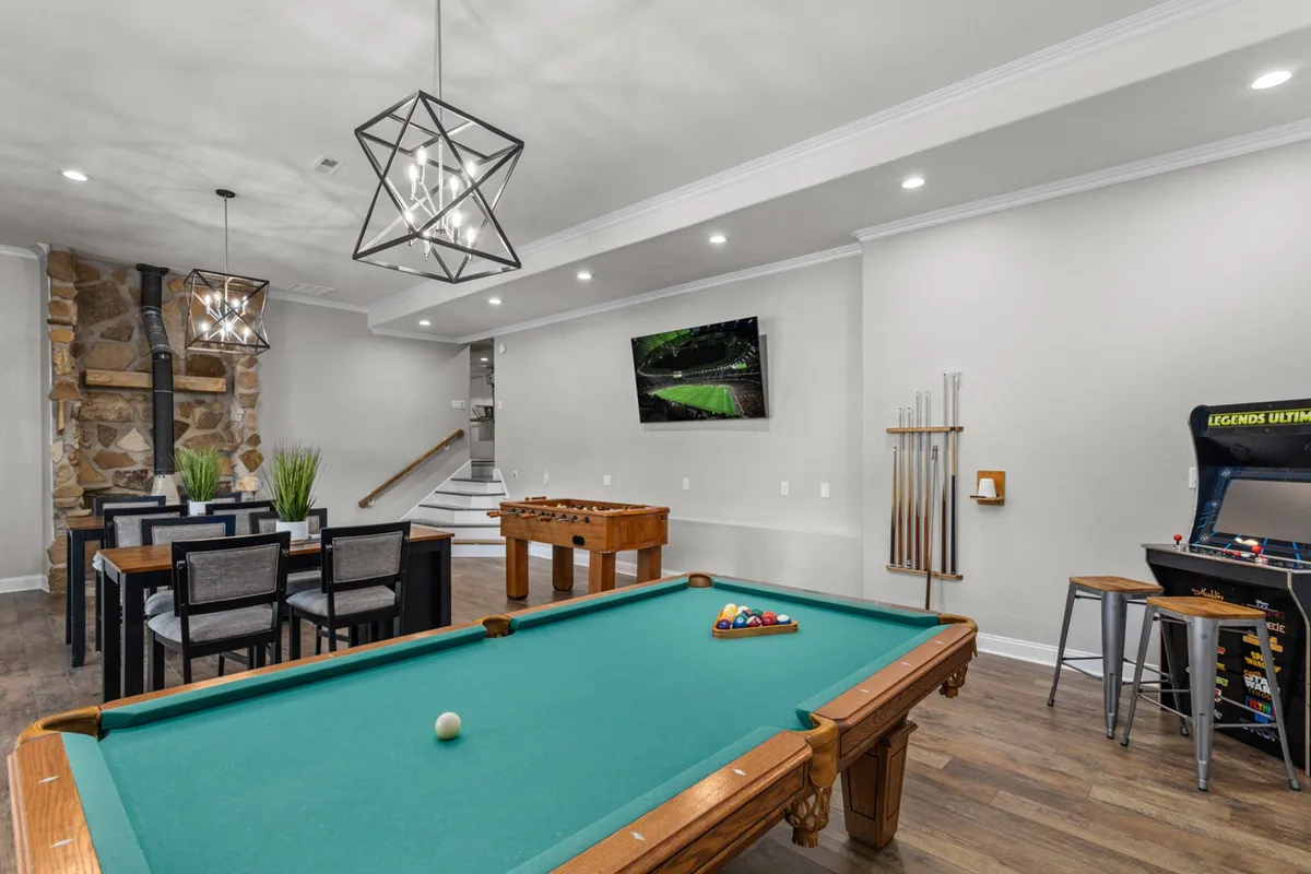 A multi-purpose entertainment space with a pool table and foosball table in the foreground, a dining area nearby, and a classic arcade machine along the wall. The open layout makes it ideal for group activities, tournaments, and casual dining, blending fun and relaxation in one seamless area.