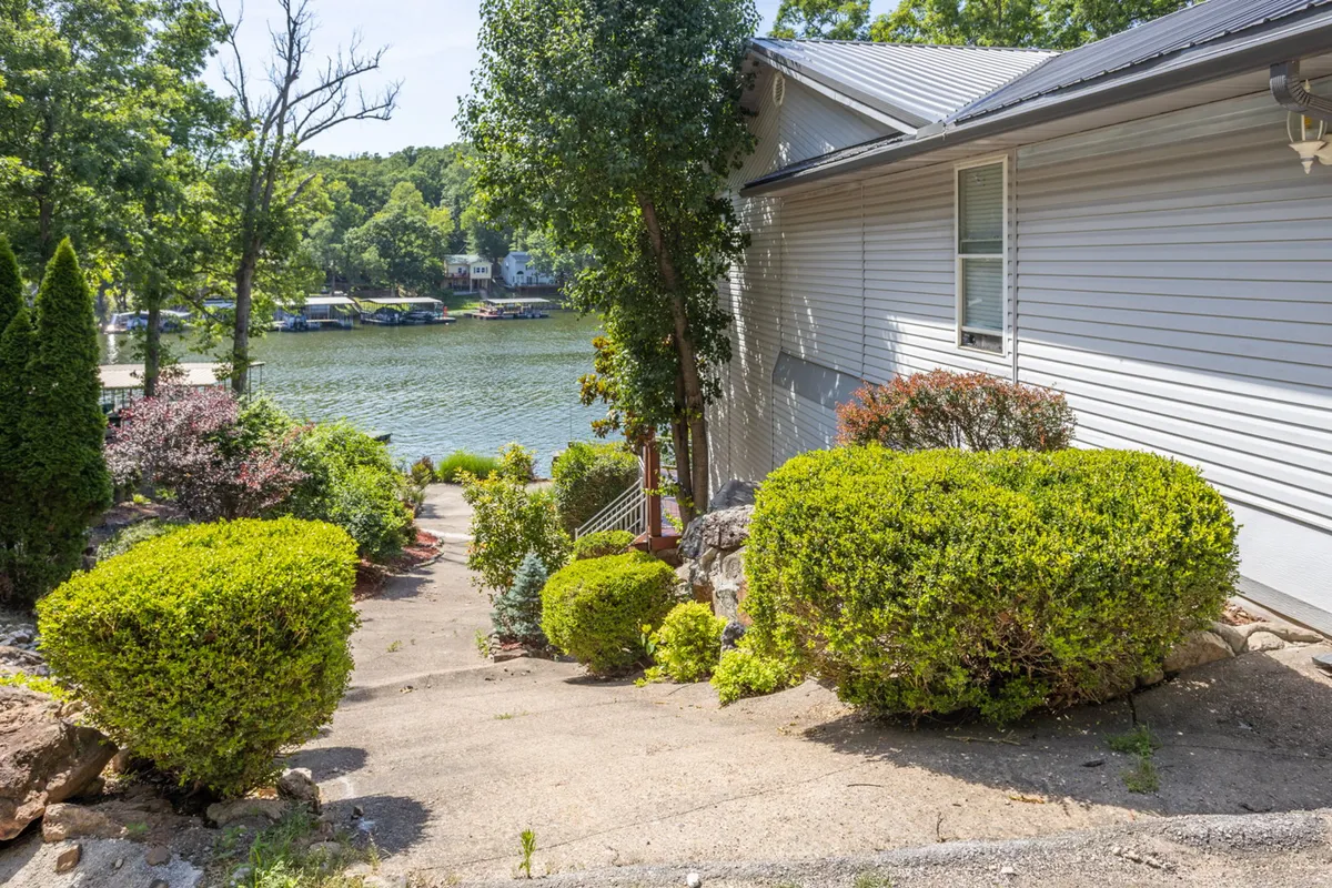 A tranquil exterior view featuring a lush green landscape, a gently winding pathway leading to the water, and a picturesque water view framed by trees. The scene evokes the peace and openness of the outdoors, inviting guests to imagine scenic walks with their pets along the shoreline and through nature.
