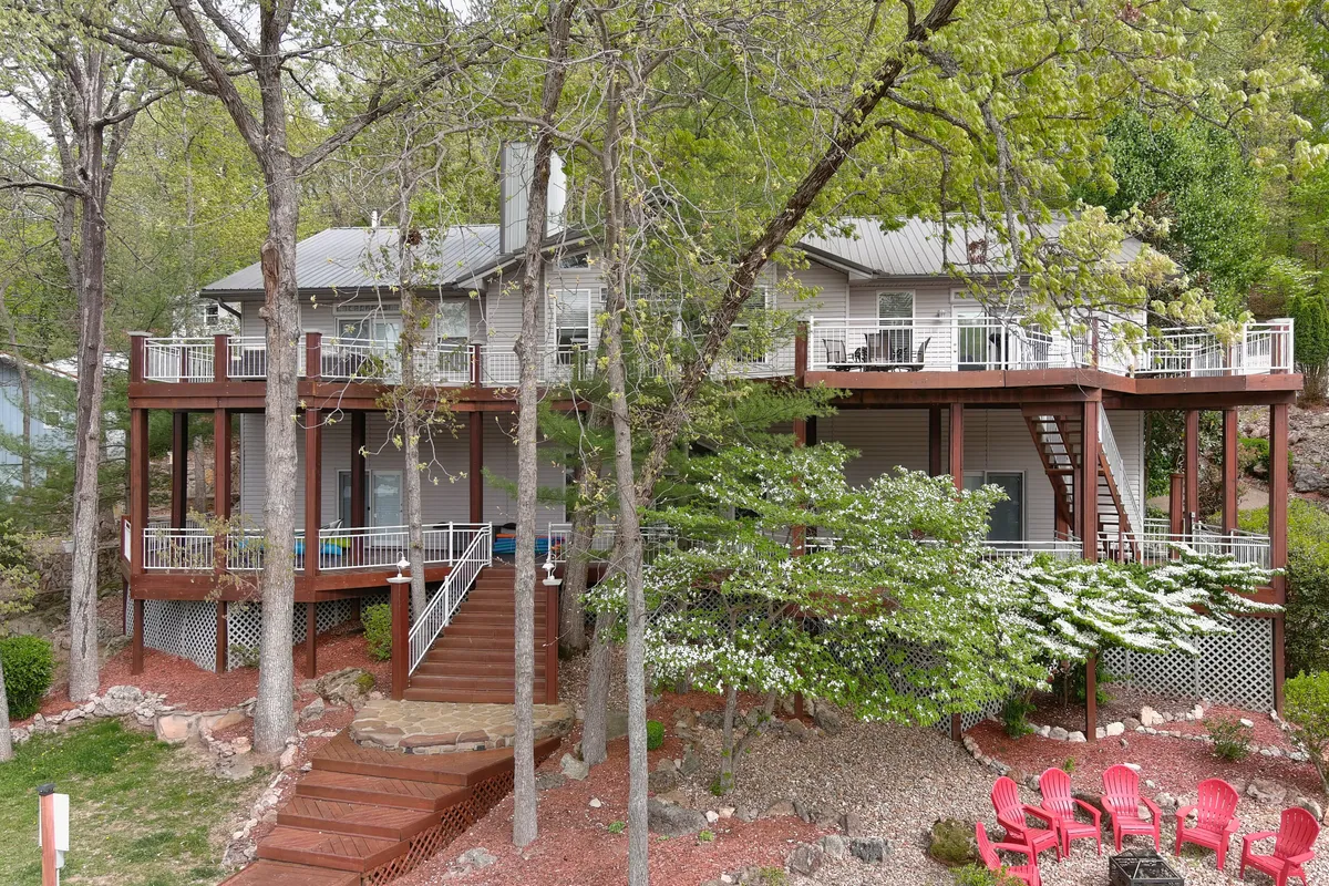 A spacious outdoor deck featuring red Adirondack chairs, a staircase leading to the yard, and surrounded by tall trees. The setting is inviting and perfectly arranged for group gatherings or relaxing evenings. The open deck offers seamless access to nature and plenty of seating for multiple guests.