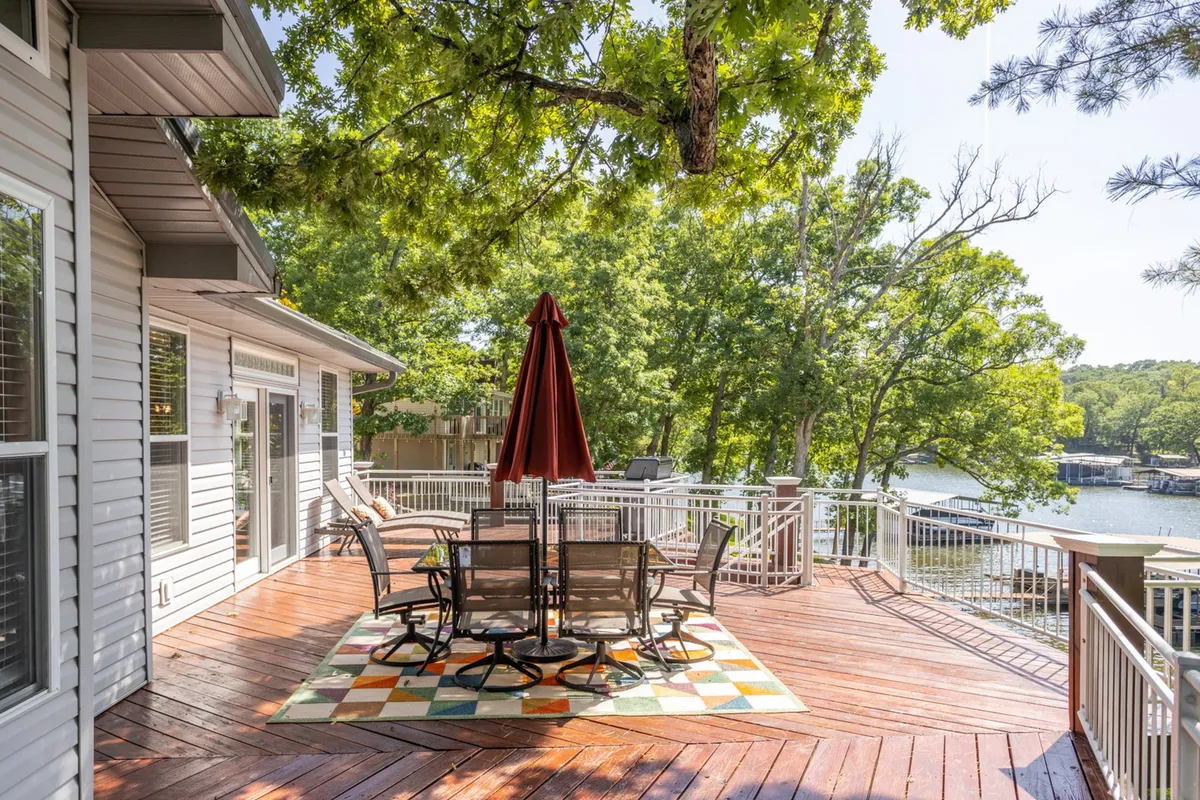 A spacious outdoor deck with an inviting dining set and a red umbrella overlooks the serene lake. The deck offers a comfortable vantage point for enjoying meals, relaxing, or savoring sweeping views of the water, especially during sunset.