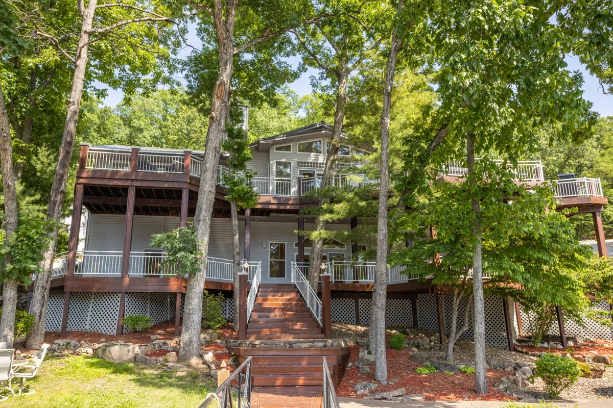A wide deck at the front entrance of the lodge, surrounded by trees and plenty of space for outdoor activities. The area is clearly set up for family barbeques, casual conversations, or simply soaking in the natural setting together.