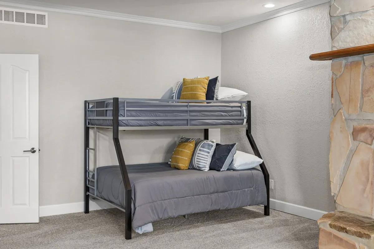A playful and inviting bedroom accented by a stylish bunk bed with decorative pillows. A stone fireplace adds warmth, and the room is decorated with cheerful touches, making it especially appealing for children and families seeking a cozy retreat.