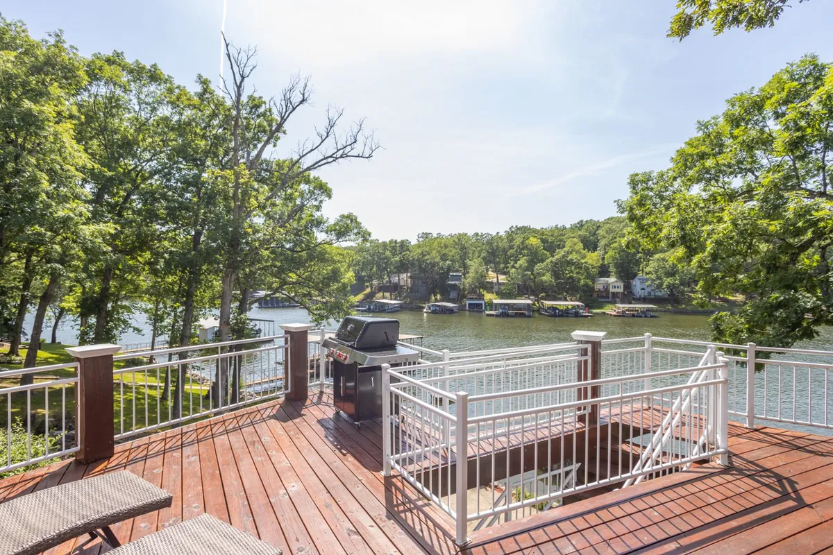 This exterior shot captures the upper deck with a grill, seating area, and a panoramic view of the lake and surrounding trees. The deck provides both shaded and sunny spots, perfect for barbecues or relaxing while enjoying the outdoors.