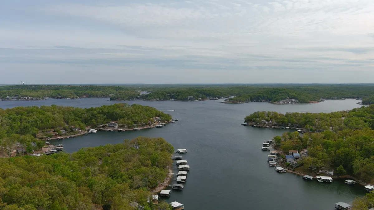 A panoramic view over calm lake waters, surrounded by greenery and distant hills, with boathouses dotting the shoreline. The atmosphere is peaceful and perfect for embracing the slower pace of the outdoors.