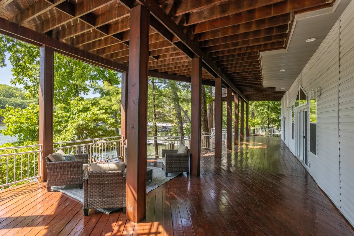 A peaceful wooden deck with wicker chairs overlooks lush greenery and a sparkling water view. This comfortable outdoor living area is a natural gathering place for both people and pets to relax and enjoy the surroundings.