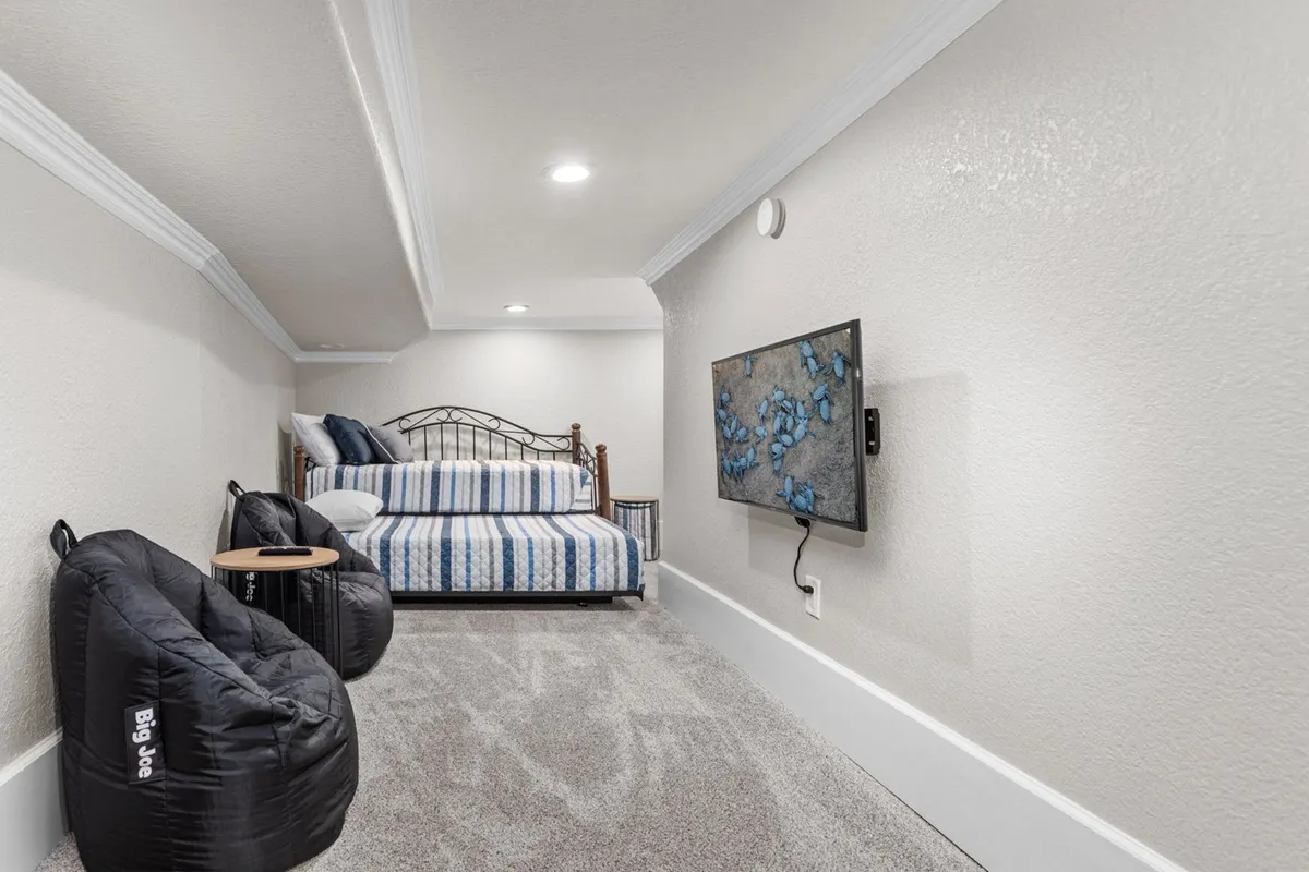 A casual downstairs bedroom featuring a twin daybed with striped bedding, colorful bean bag chairs, and a wall-mounted TV. The room is designed for relaxation and fun, catering especially to younger guests or those looking for a cozy nook to unwind.