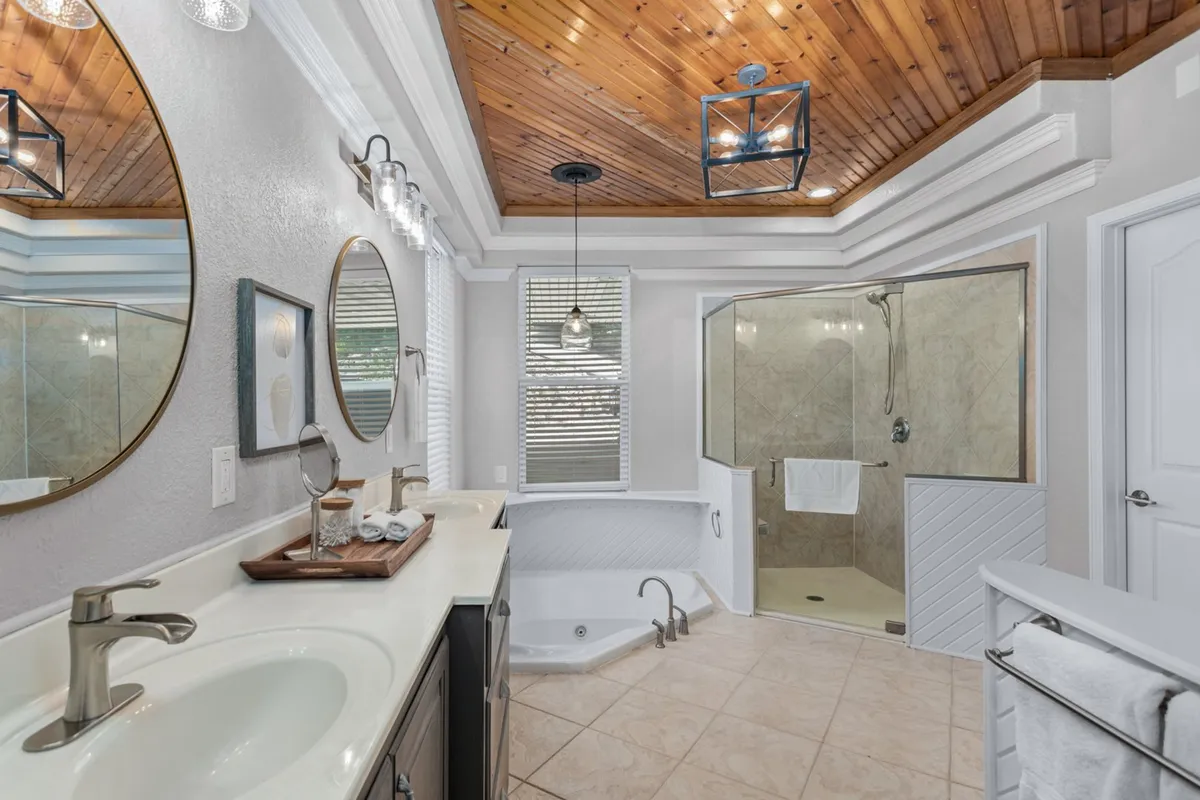A luxurious bathroom featuring a freestanding jetted bathtub, large mirrors, a separate shower area, and decorative light fixtures. The space feels spa-like, with warm wooden ceilings and clean lines, offering guests the perfect spot to unwind after a day by the lake.
