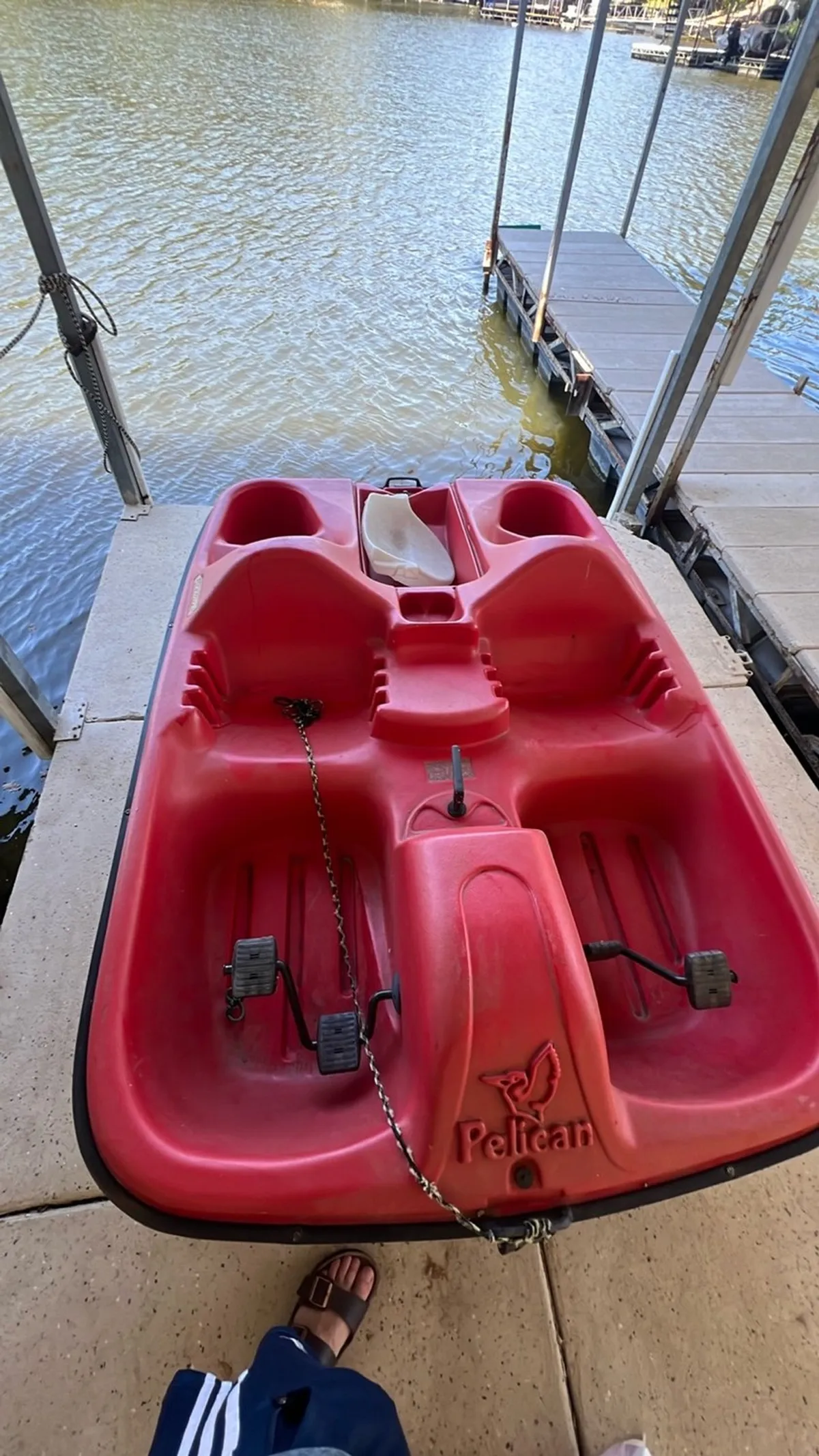 A vibrant red paddle boat sits beside the dock, with calm lake water reflecting the sky. The scene feels playful and inviting, suggesting opportunities for paddle boating, fishing, or simply enjoying the lakeside environment with family and friends.