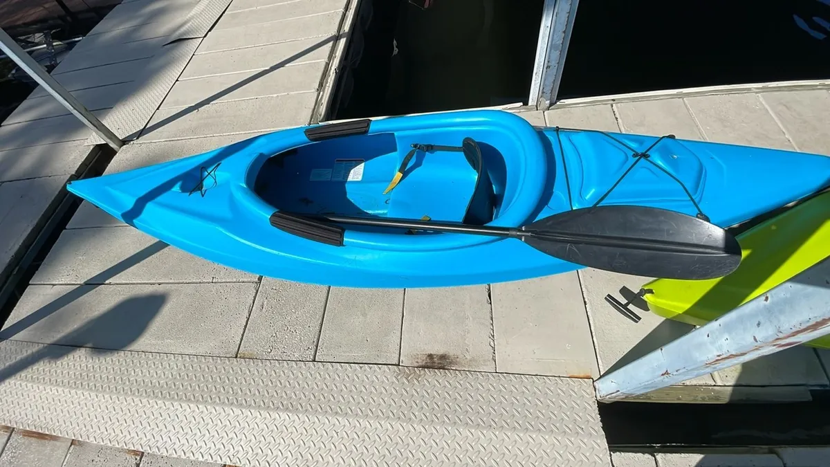 This image showcases a blue kayak resting on the dock, with tranquil water stretching out into a peaceful cove. The dock is central, inviting guests to launch into the lake for kayaking, fishing, or enjoying the scenery. The setting sun casts a warm glow across the water, enhancing the serene, adventurous atmosphere.